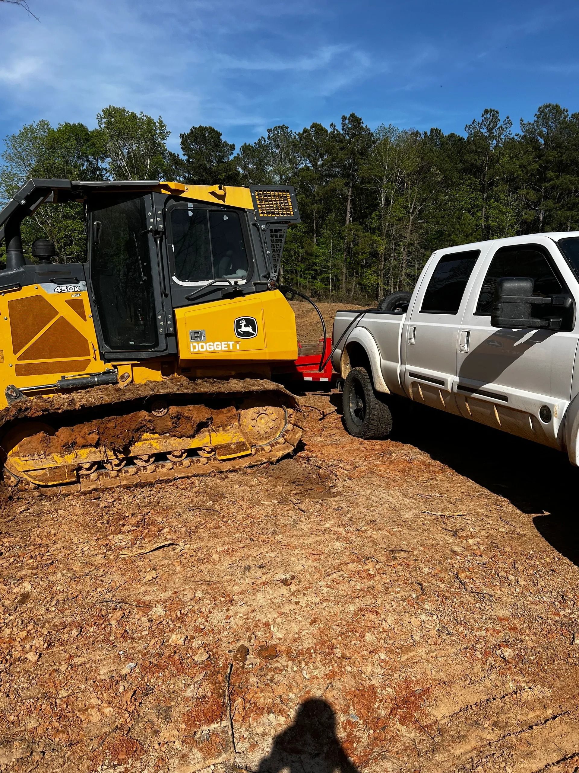 A white pickup truck towing a yellow John Deere bulldozer on a construction site.