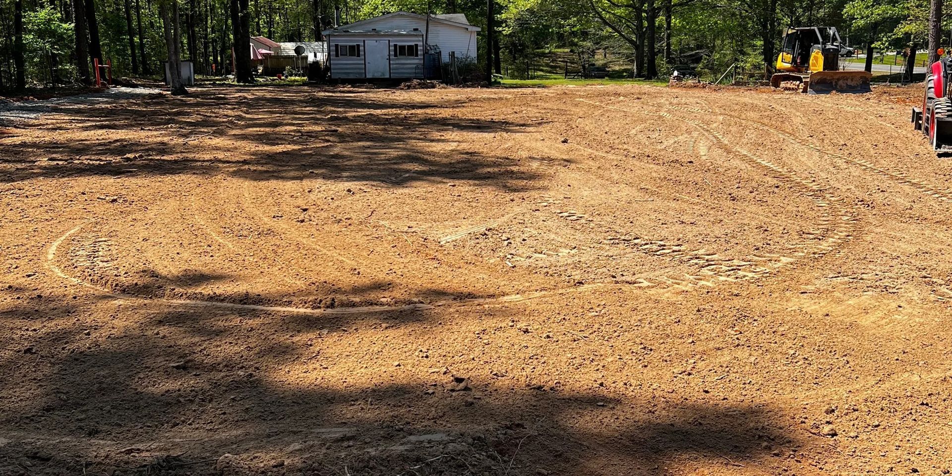 A cleared dirt area with a trailer in the background and an excavator on the right.