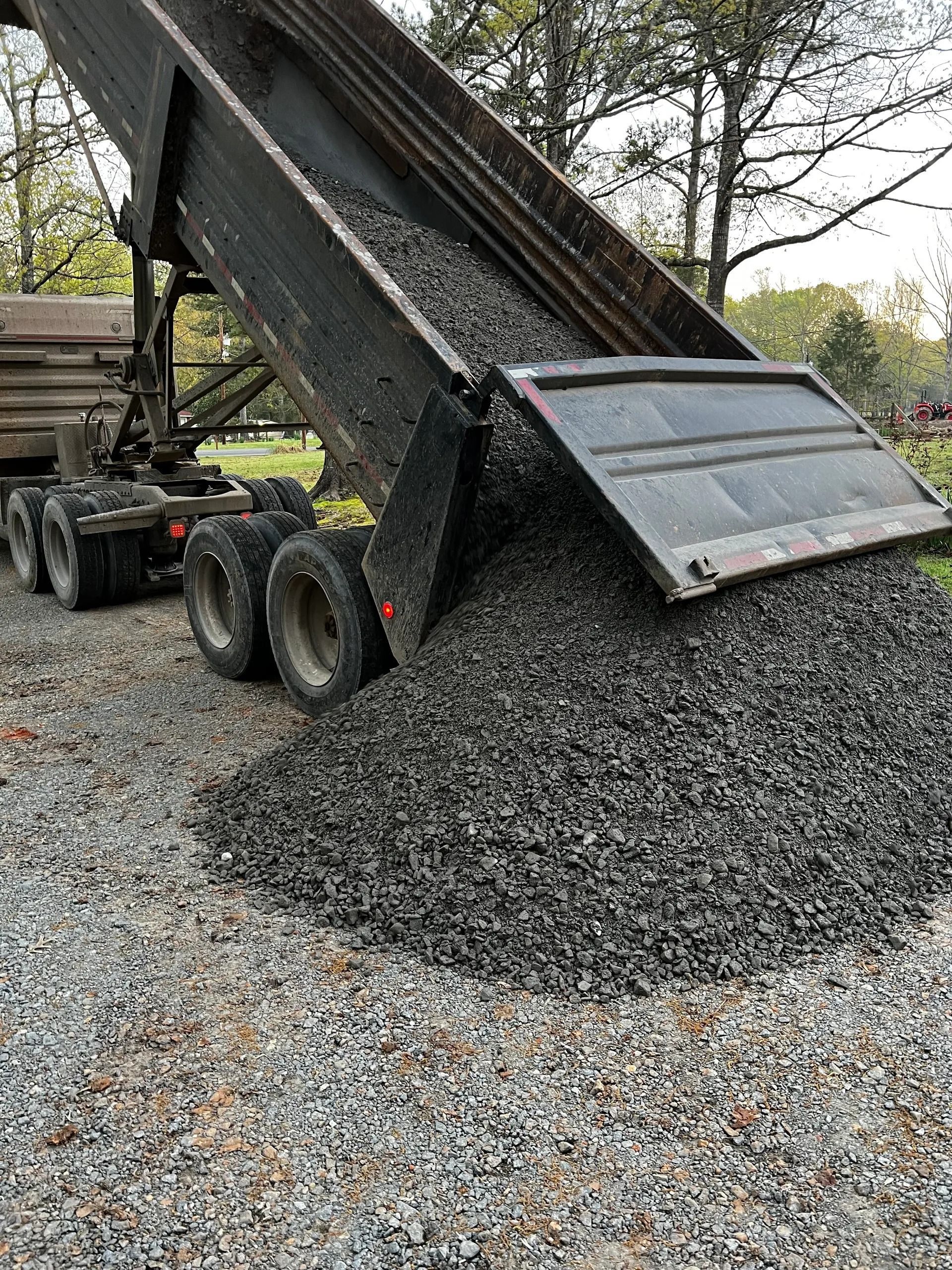 Dump truck dumping gravel onto a gravel driveway.