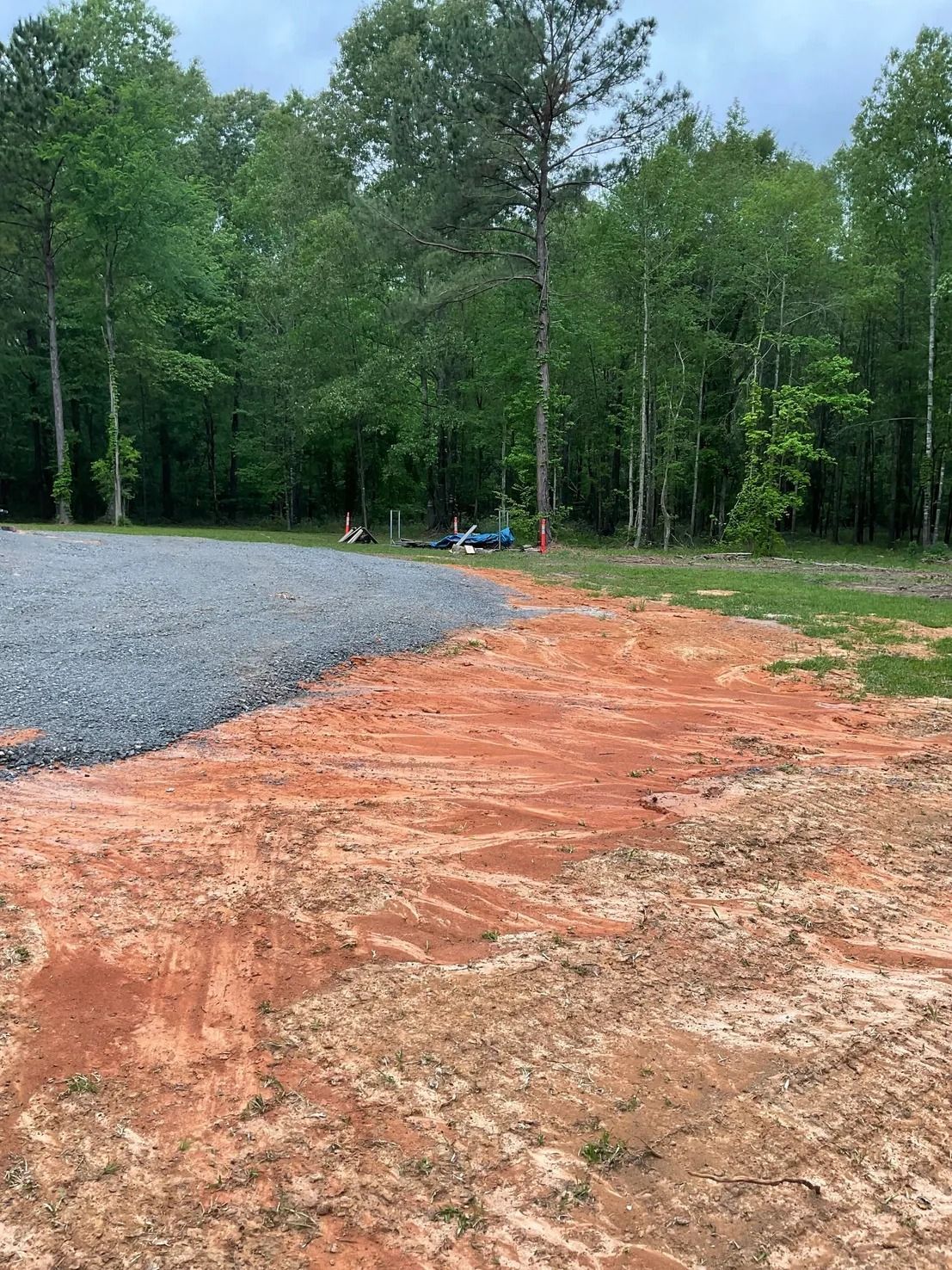 Gravel and reddish-brown soil meet in a yard, trees in the background under an overcast sky.
