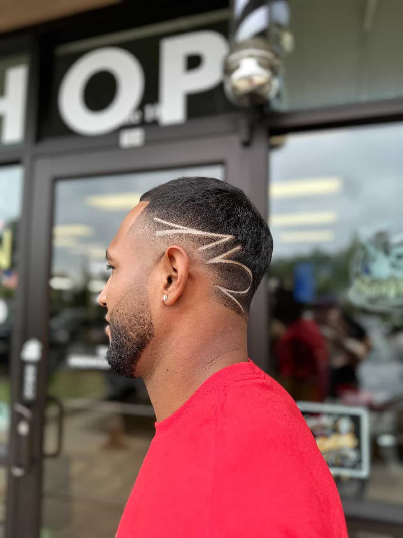Barber trimming a man’s fade haircut in a barbershop.