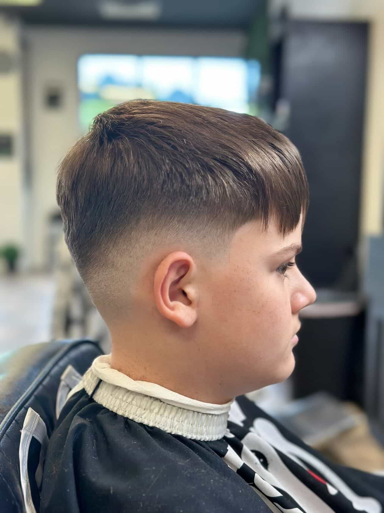 Barber trimming a child’s hair with electric clippers in a salon.