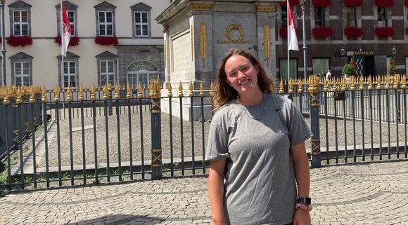A woman is standing in front of a fence in front of a building.