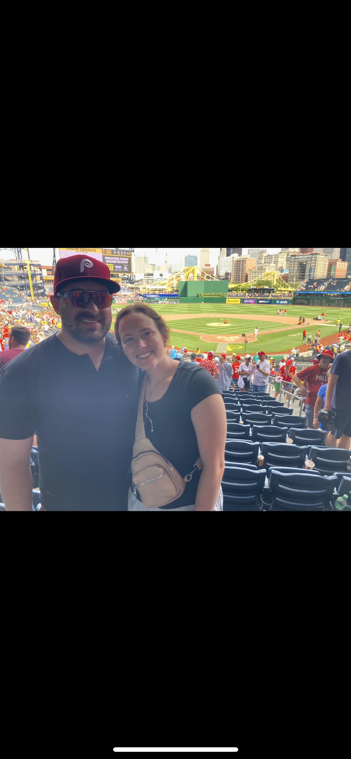 A man and a woman are posing for a picture at a baseball game.