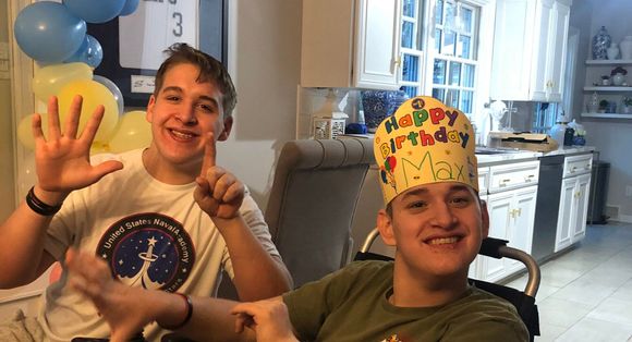 Two boys wearing birthday hats are sitting next to each other in a kitchen.