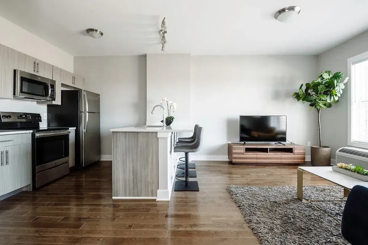 A living room with hardwood floors and a kitchen with stainless steel appliances.
