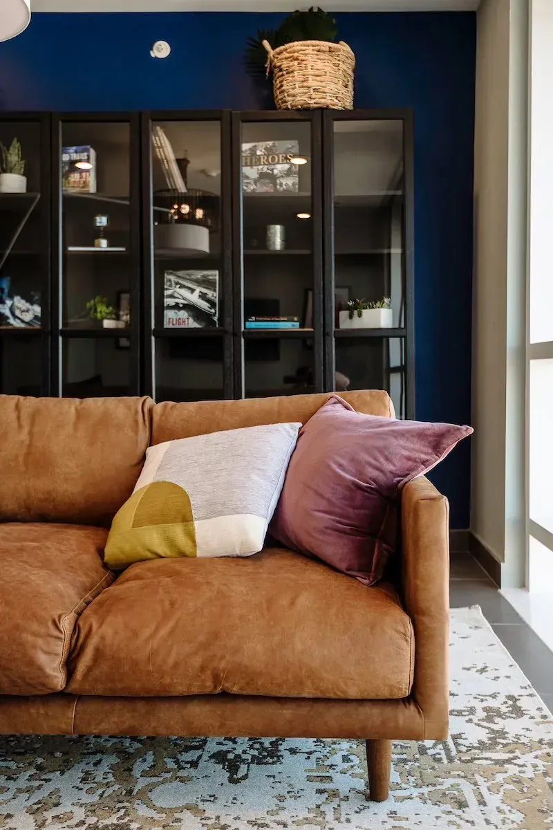 A living room with a brown leather couch and pillows.