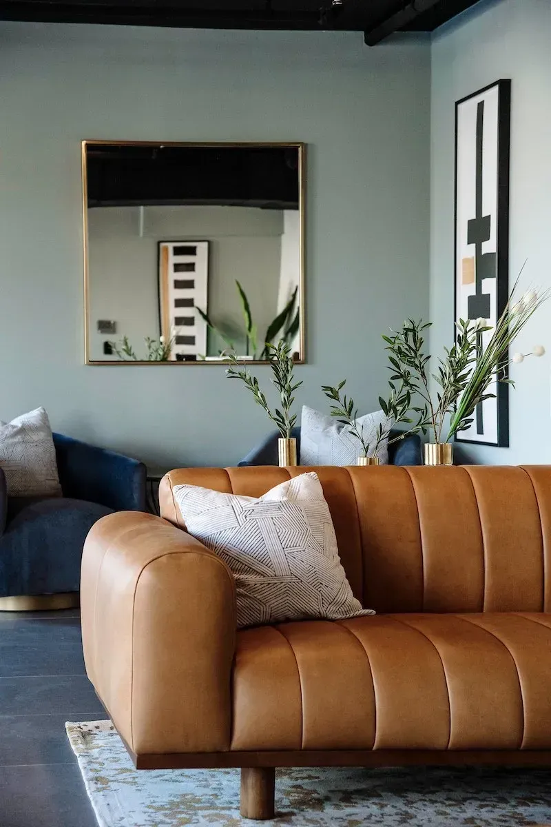 A living room with a brown leather couch and a mirror.