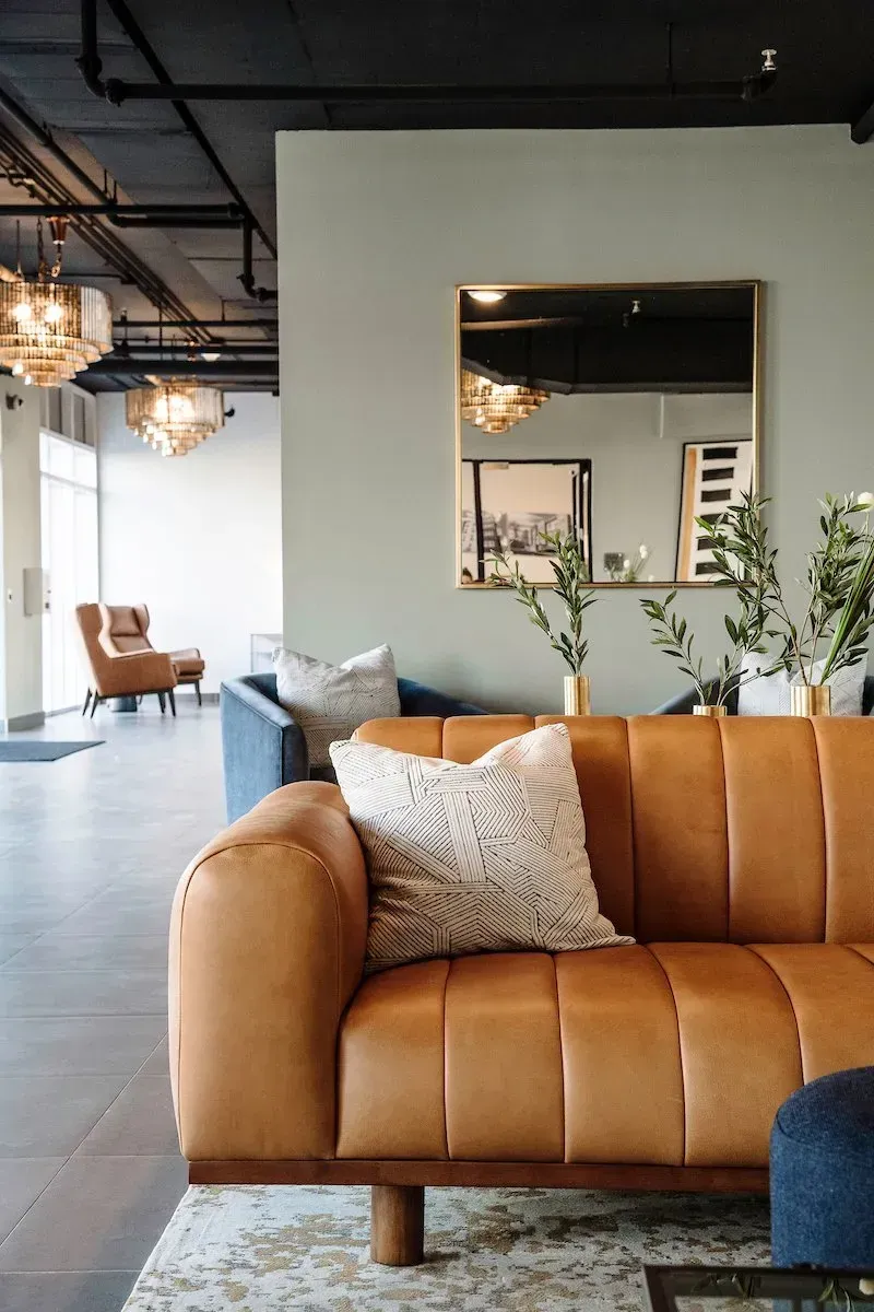 A living room with a brown leather couch and a mirror.