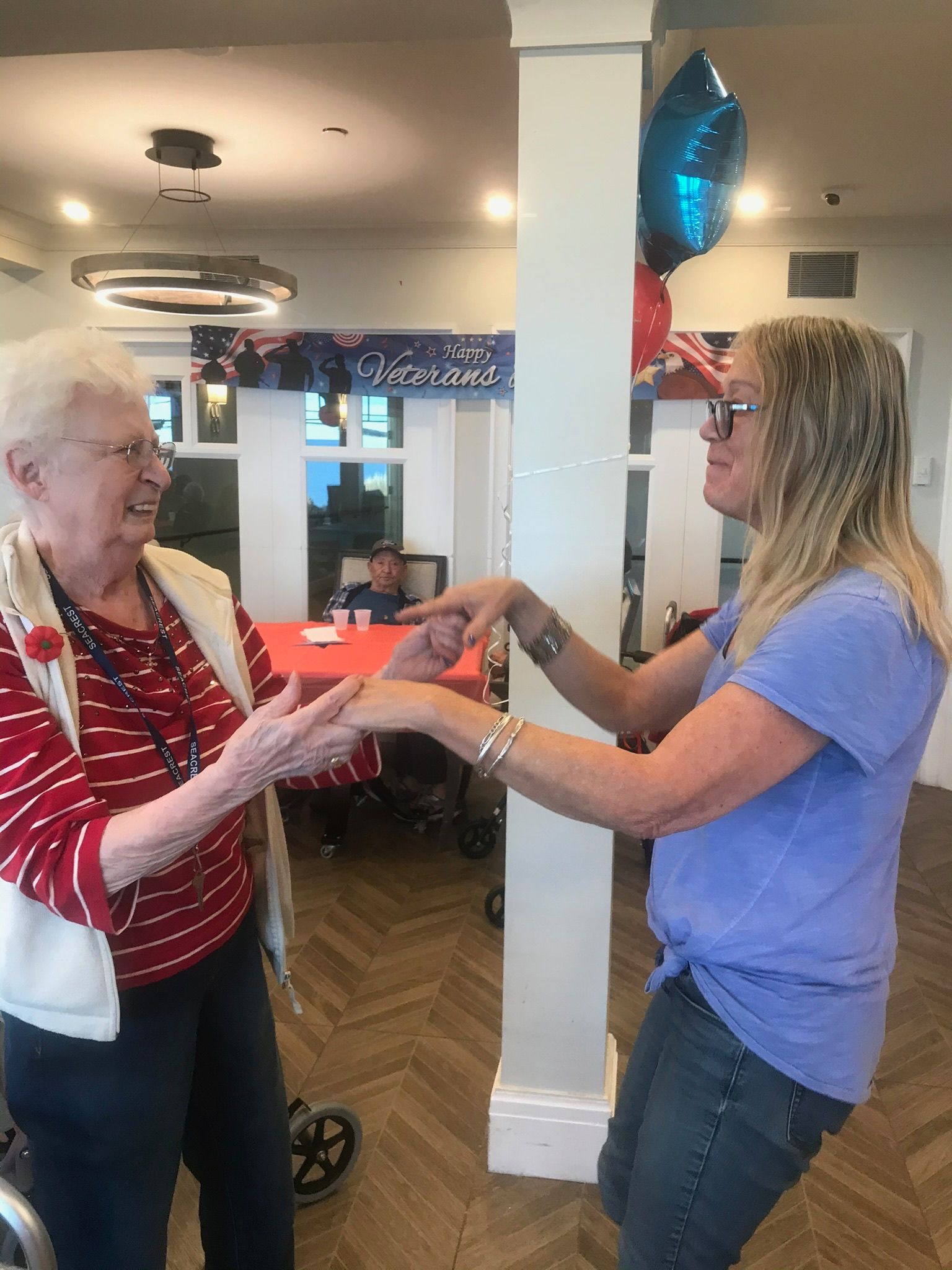 Two women smiling, dancing indoors. Red, white, and blue decor.