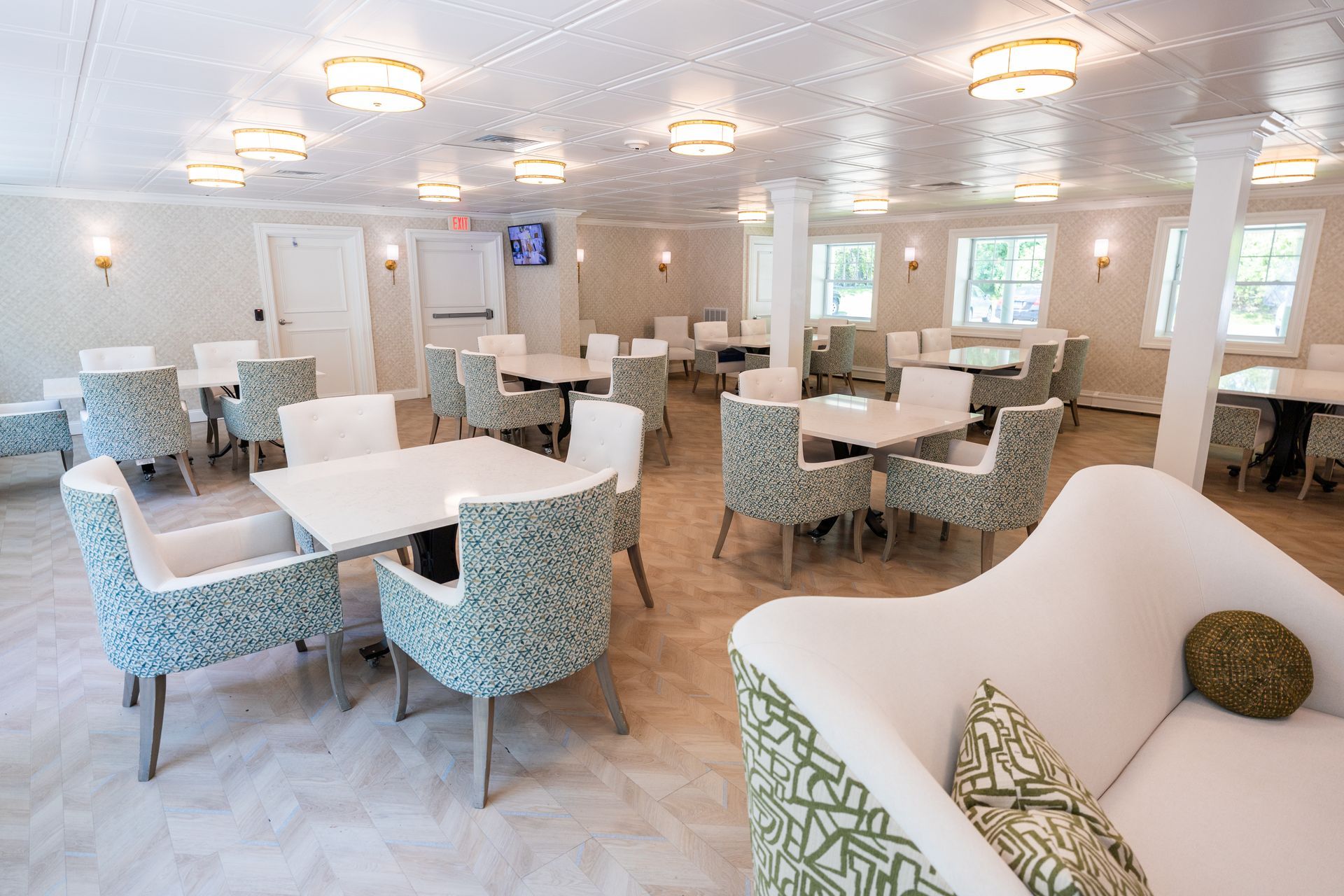 Bright, modern dining room with white tables, blue patterned chairs, and a sofa seating area