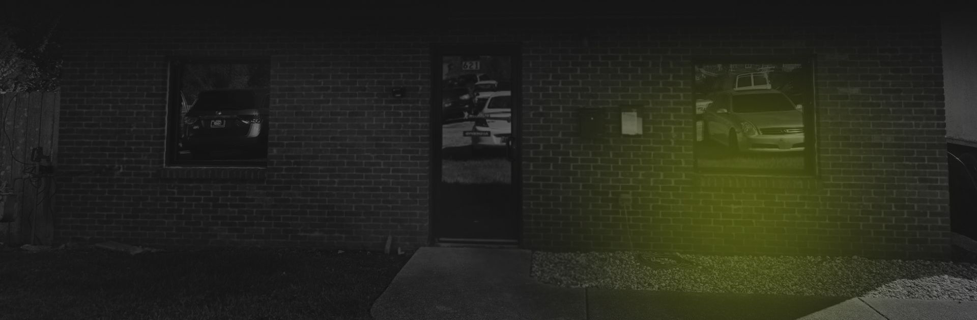 Brick building with two windows and a door reflecting a car. Dark lighting. | Spring Hill Automotive Center