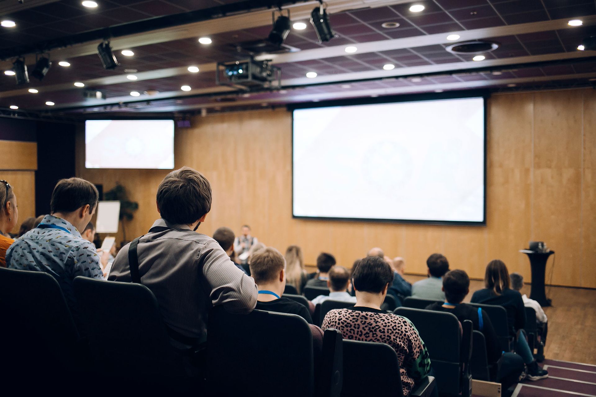 A group of people are sitting in an auditorium watching a presentation on a large screen.