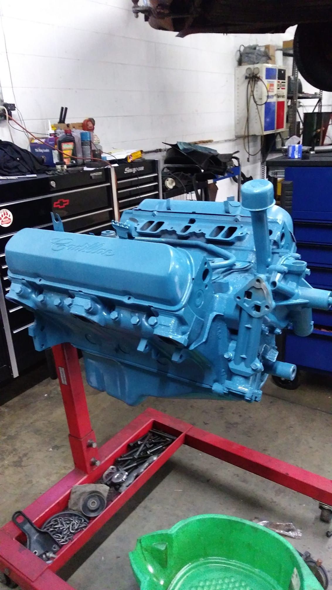 A blue engine is sitting on a red stand in a garage.