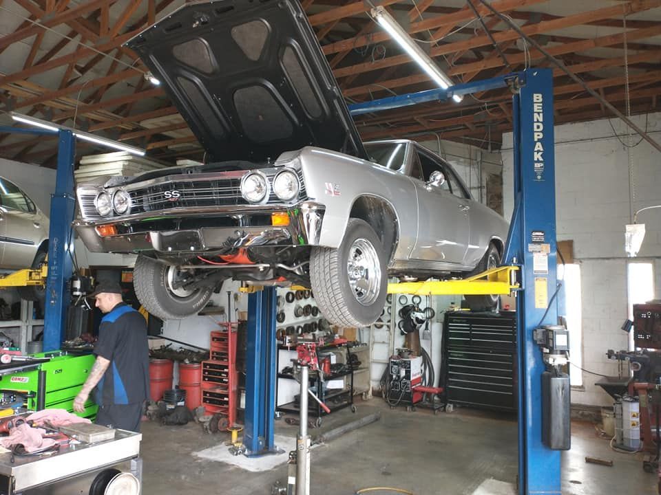 A car is sitting on a lift in a garage with the hood up.