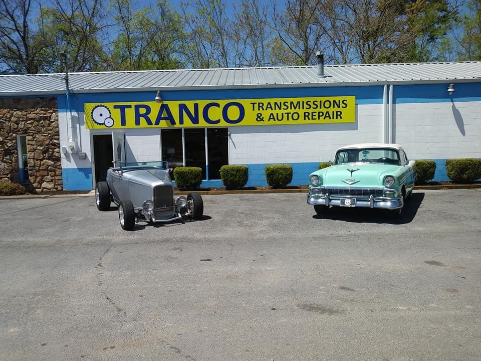 Two cars are parked in front of a tranco transmissions and auto repair shop