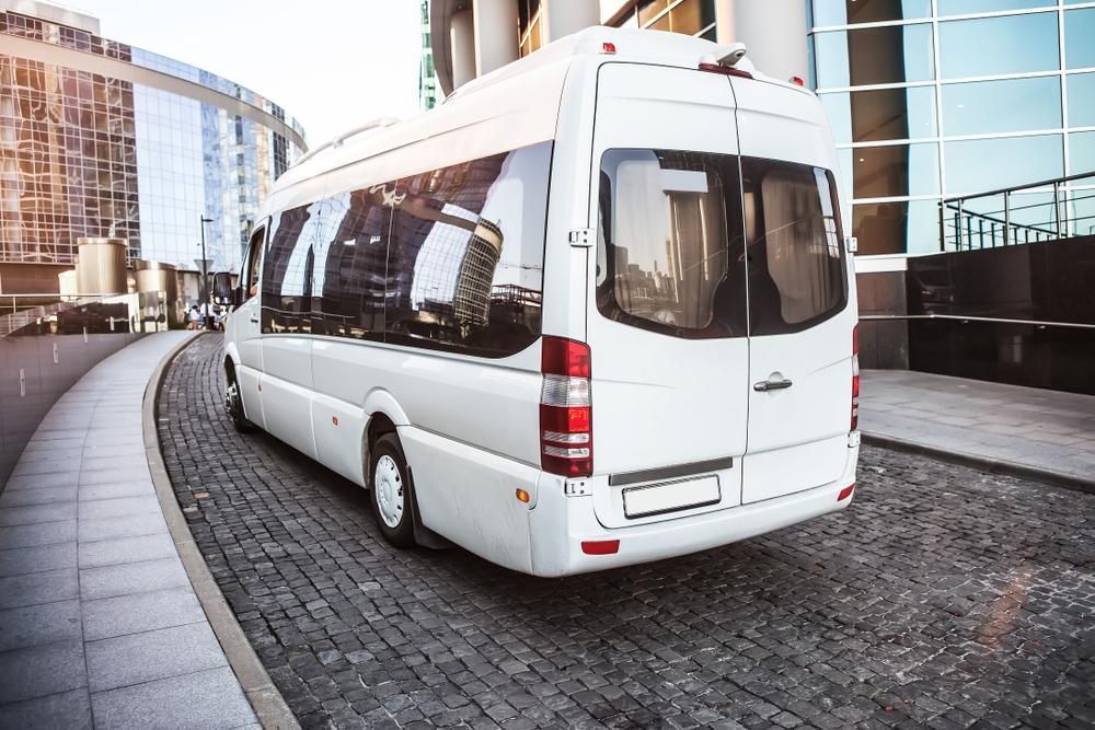A White Bus Is Driving Down A Cobblestone Street In Front Of A Building — Whitsunday Transfer Service In Cannonvale, QLD