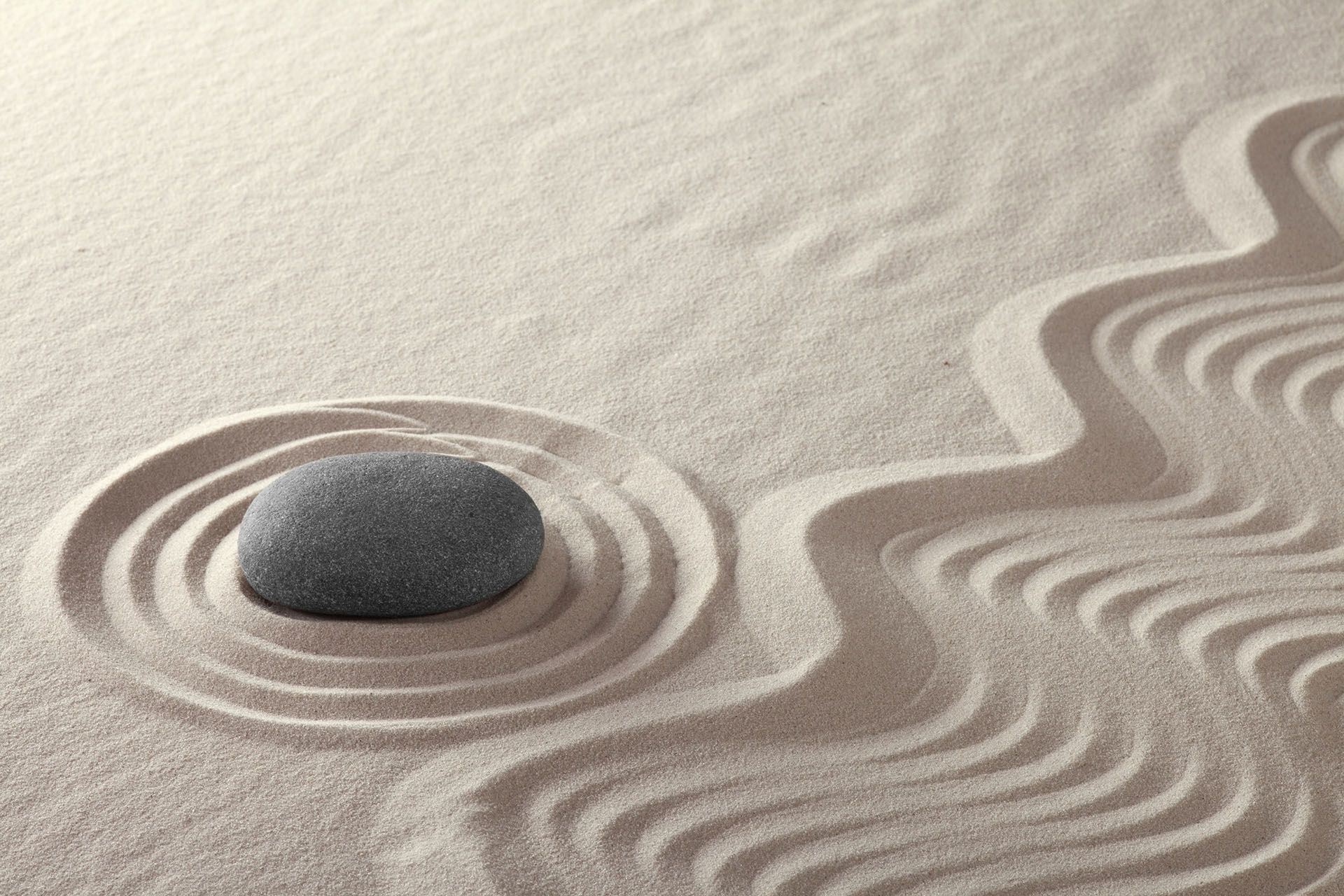 Smooth gray stone in a bed of raked sand with swirling patterns and concentric circles.