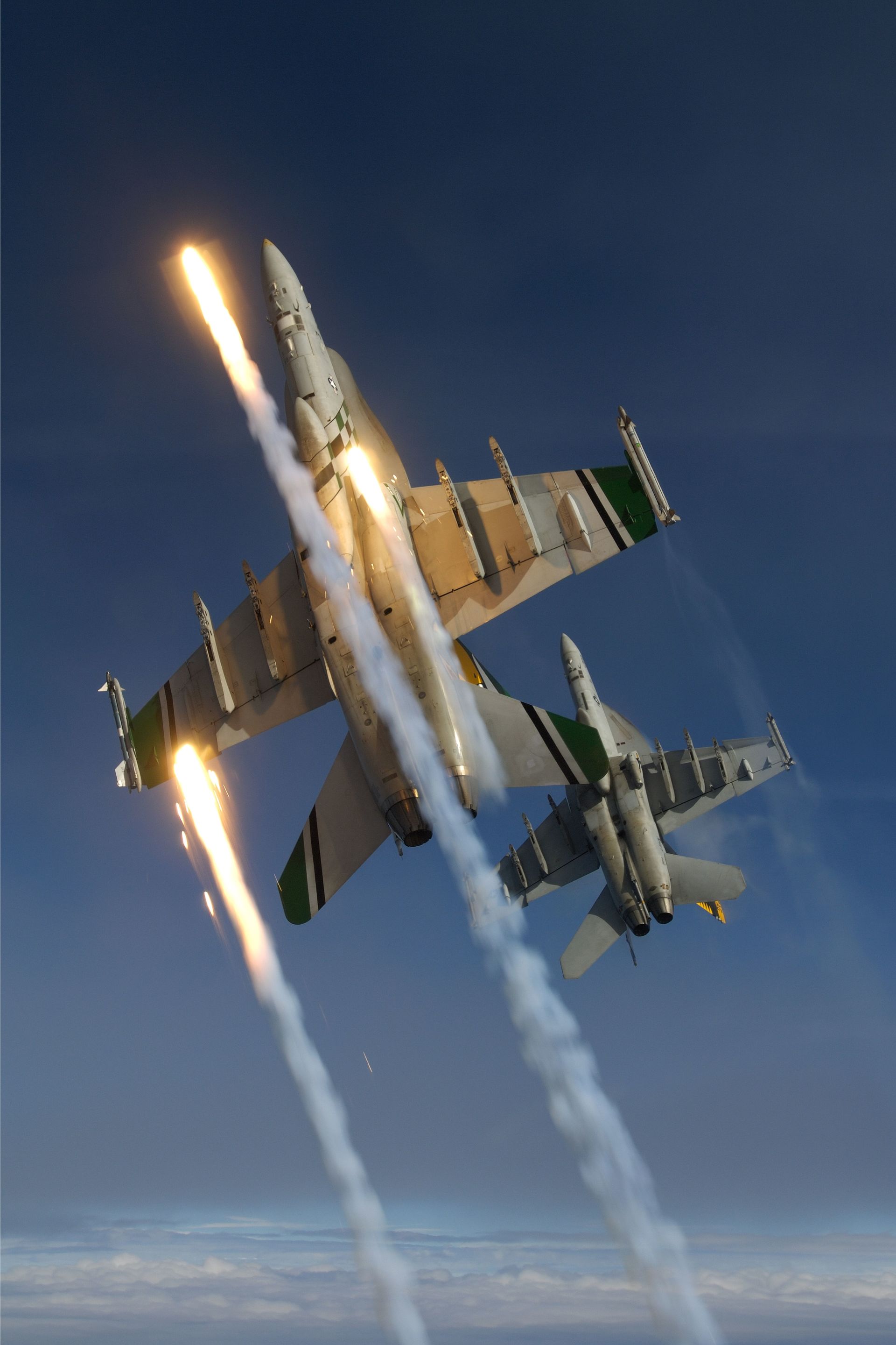 Two fighter jets are flying in the sky with smoke coming out of their wings.