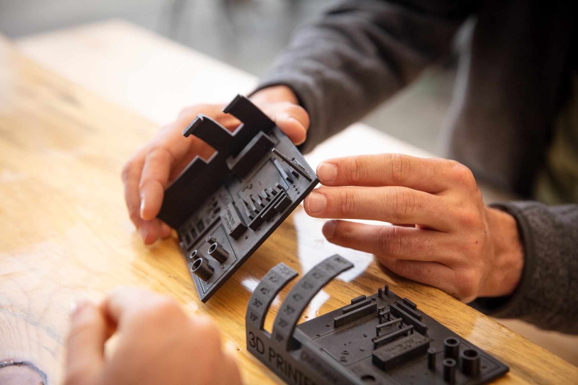 A person is holding a piece of black plastic on a wooden table.