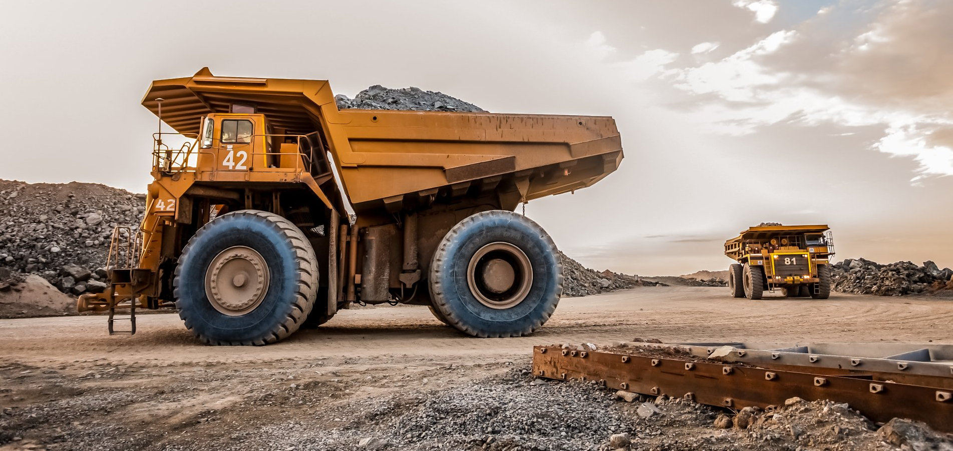 Two dump trucks are parked next to each other on a dirt road.
