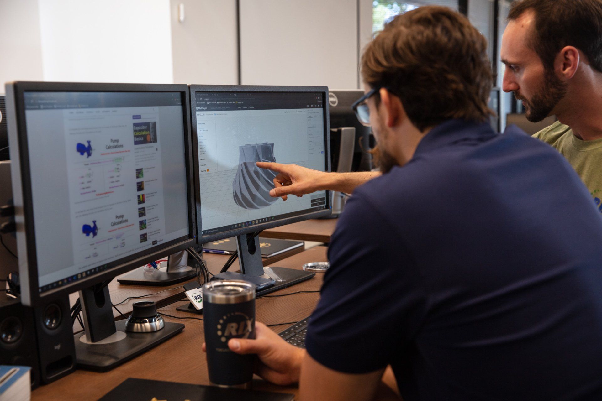 Two men are sitting at a desk looking at a computer screen.