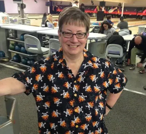 A woman in a bowling alley wearing a shirt with crossbones on it A woman in a bowling alley wearing a shirt with crossbones on it