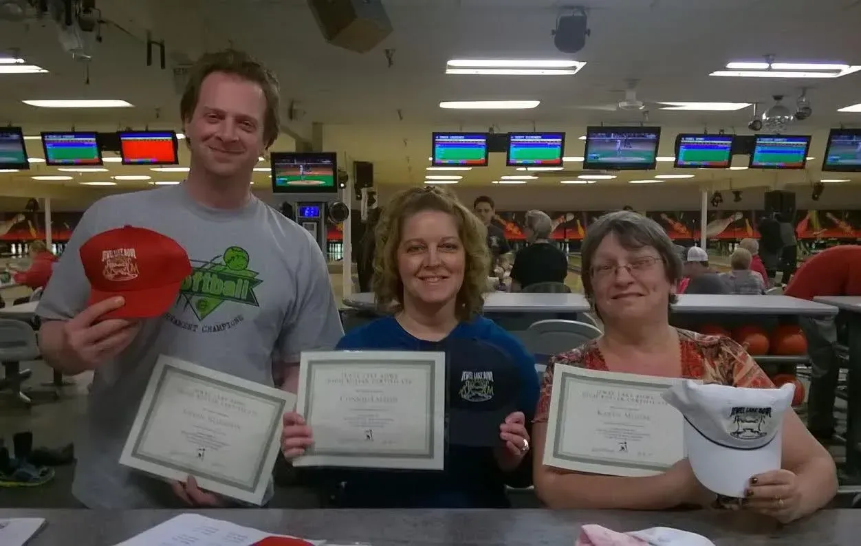 Three people holding certificates and hats in a bowling alley Three people holding certificates and hats in a bowling alley