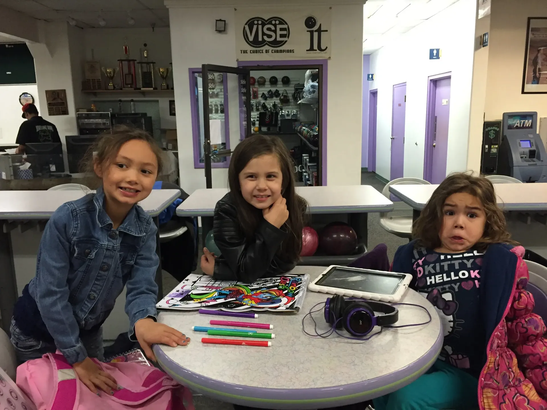 Three young girls are sitting at a table with a sign that says vise it Three young girls are sitting at a table with a sign that says vise it