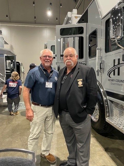 Two men are posing for a picture in front of a fire truck.