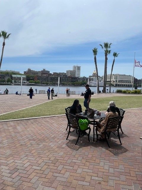 A group of people are sitting around a table in front of a body of water.