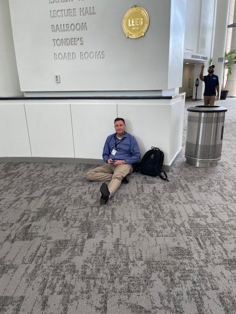A man is sitting on the floor in front of a sign that says lecture hall