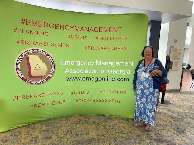 A woman is standing in front of a green sign that says emergency management association of georgia