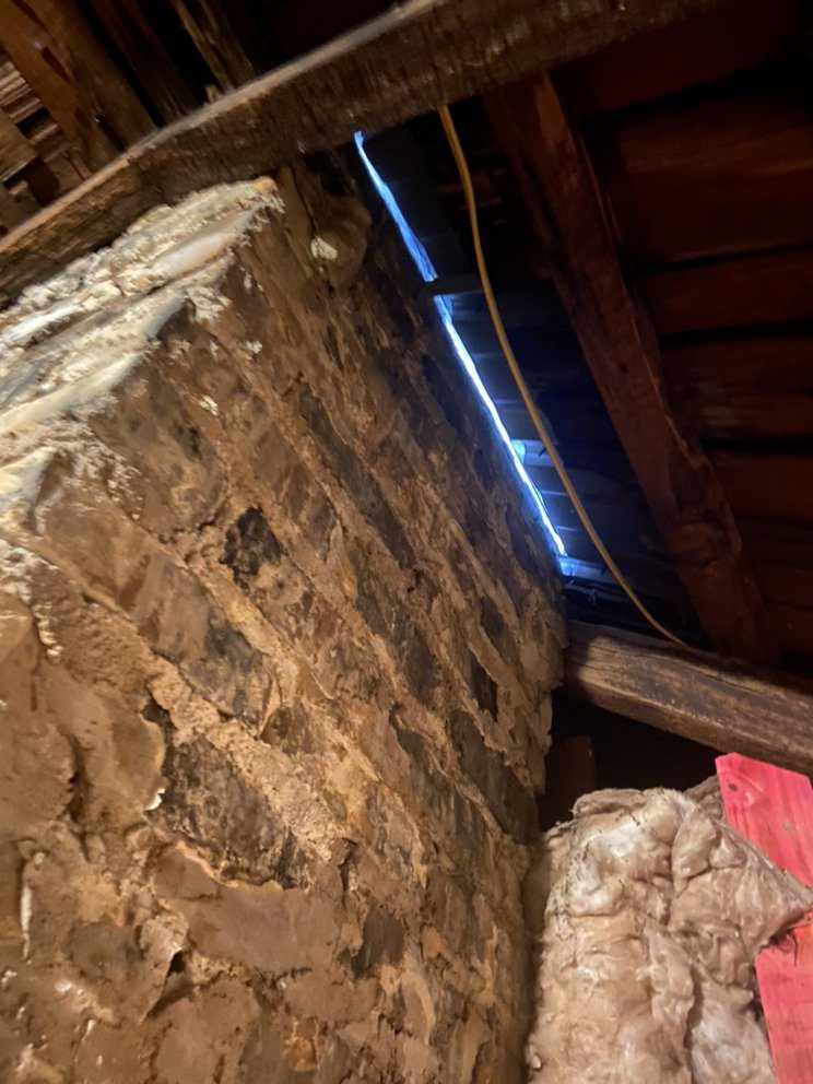Brick chimney in attic, gap near roof. Old insulation visible.
