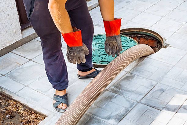 Person with gloves and sandals near open manhole with hose.