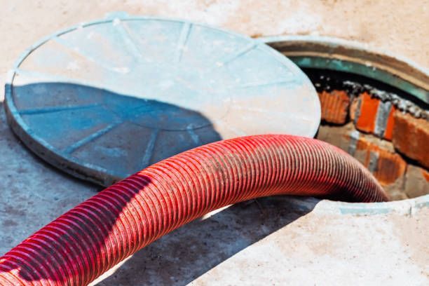 Red hose emptying into open manhole with lid nearby.