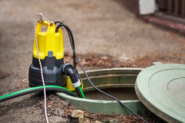 Yellow and black submersible pump in an open, green manhole, with hoses.