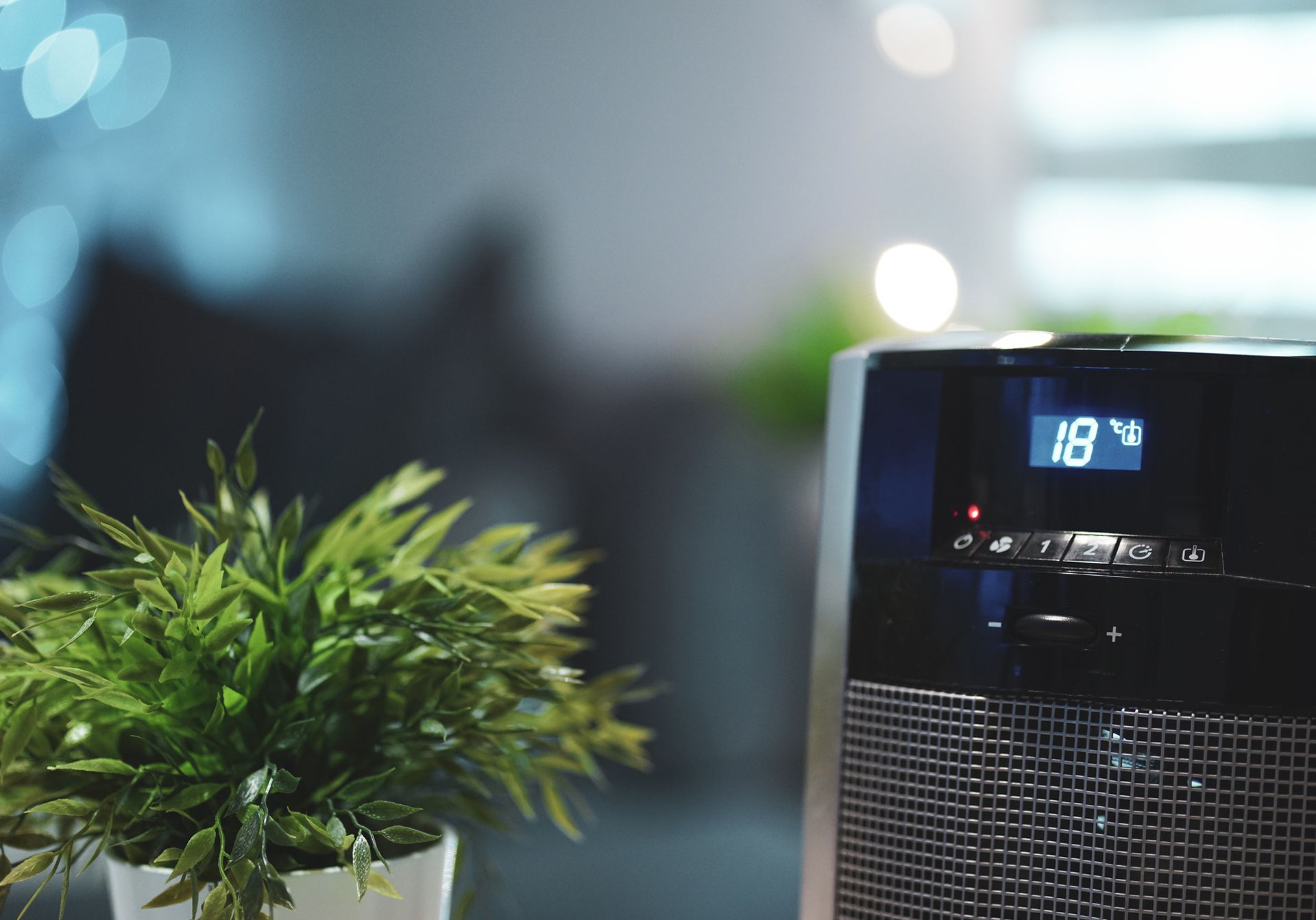 Black space heater with digital display showing 18 degrees, next to a potted plant; interior shot.