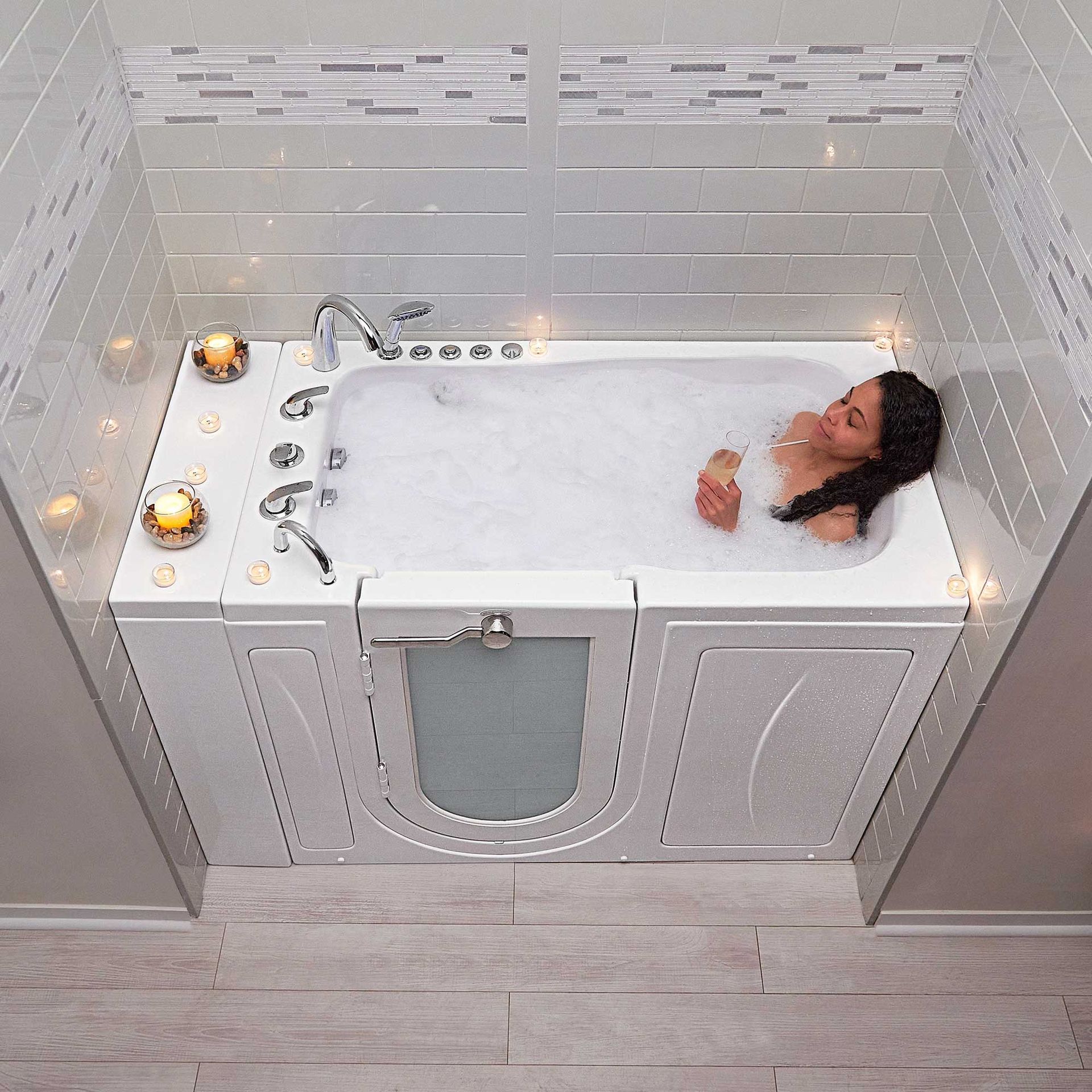 A bathroom with a bathtub , sink and mirror. A woman is laying in a bathtub filled with bubbles
