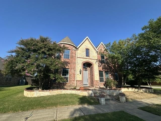 Two-story brick house with tan accents, arched entry, tower, and landscaped yard on a sunny day.