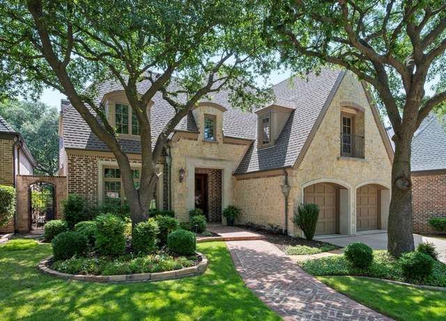 Two-story house with brick walkway, stucco walls, arched dormers, and lush landscaping.