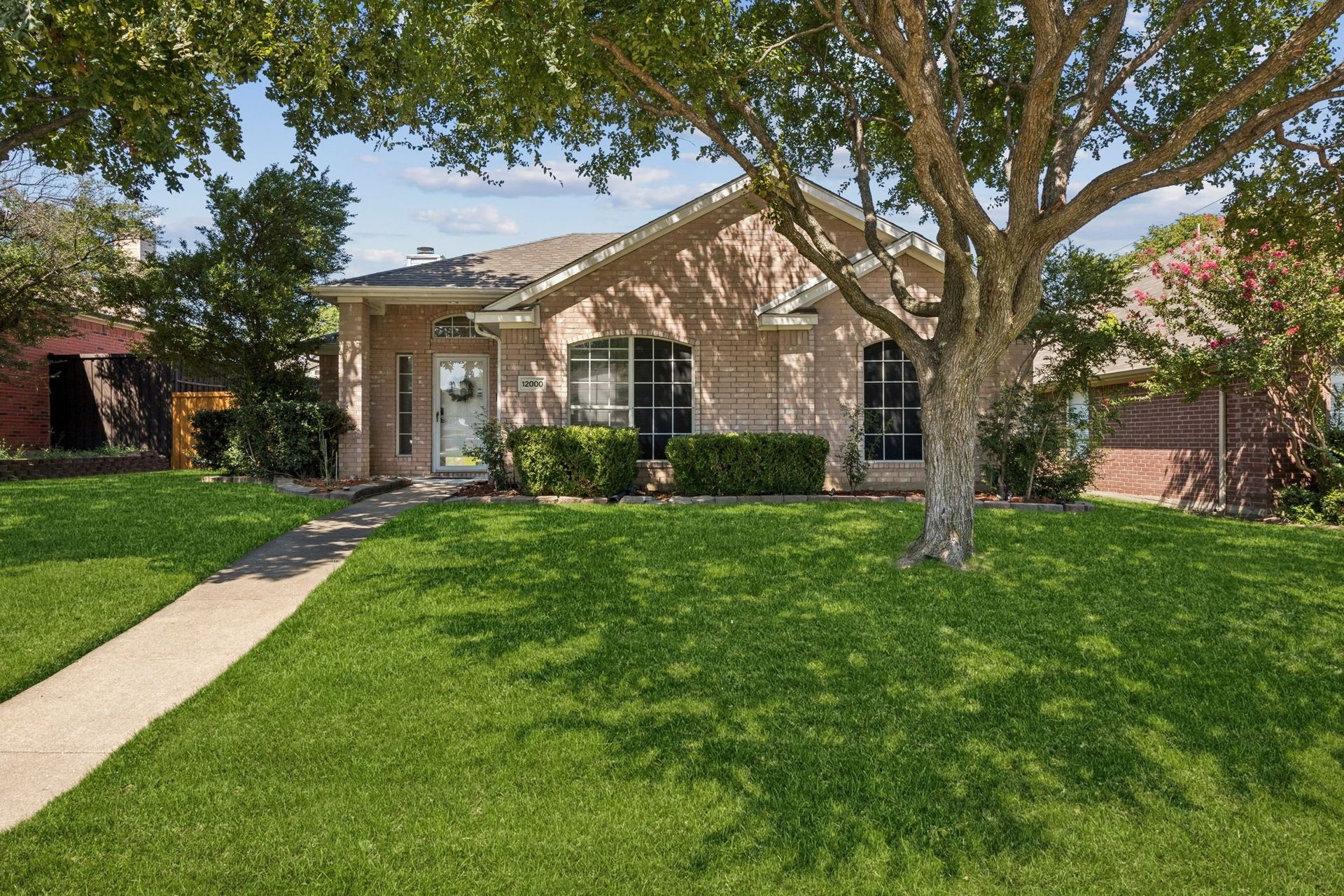Tan brick house with green lawn, tree, and sidewalk.