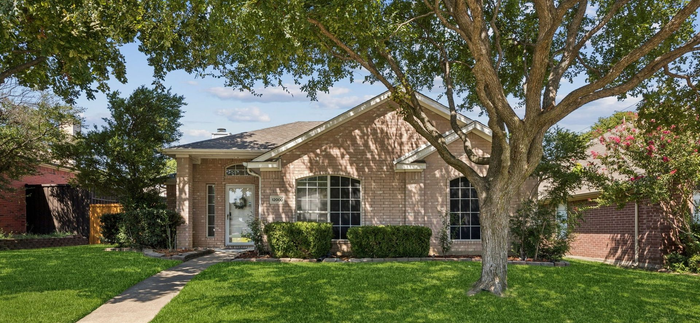 A brick house with a green lawn and a large tree in front.