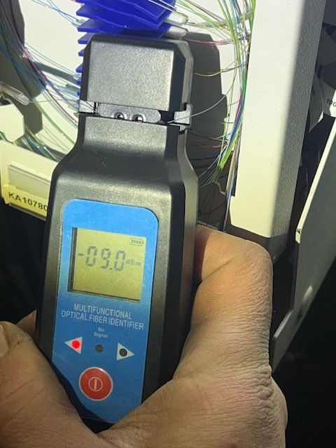 Käsi, jossa on mustaa ja sinistä optista kuitutunnistinta, joka näyttää lukeman -09,0 dB.