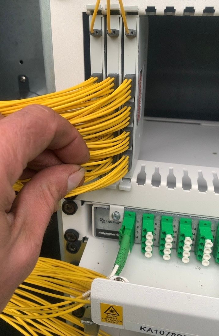 Käsi koskettaa keltaisia valokuitukaapeleita verkkoräkissä, vihreät liittimet näkyvissä.