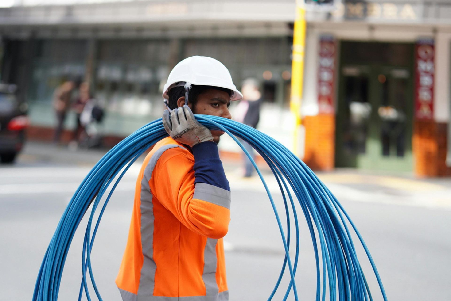 A man wearing a hard hat is carrying a bunch of blue wires.