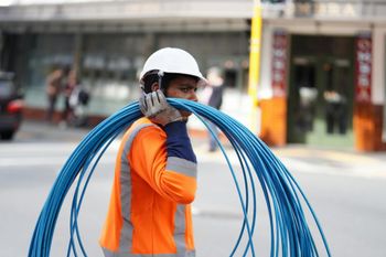 A man wearing a hard hat is carrying a bunch of blue wires.
