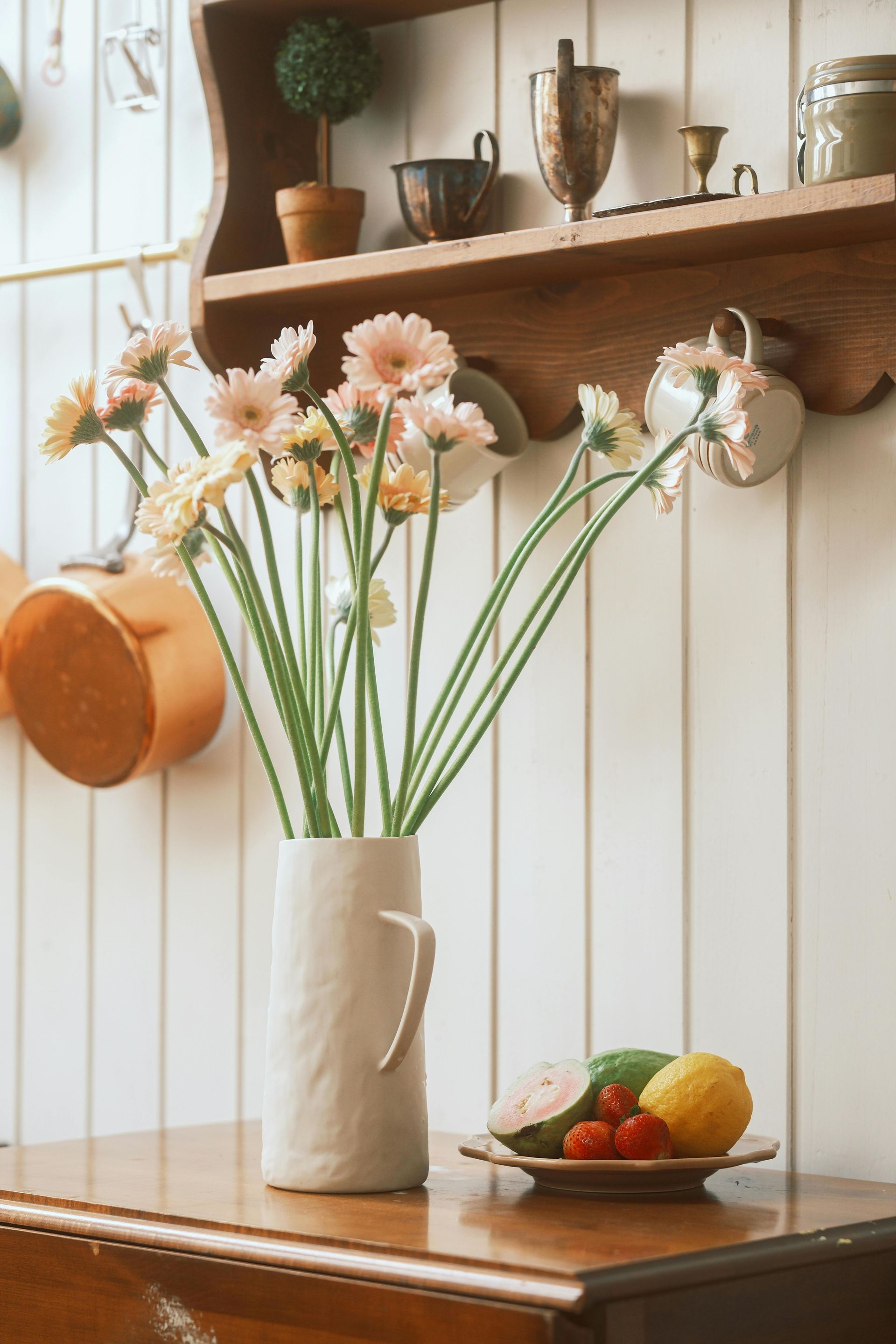 A vase of flowers sits on a wooden table next to a plate of fruit.