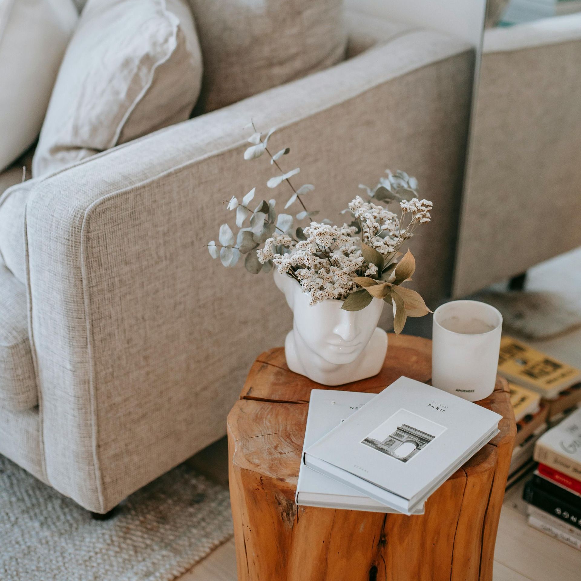 A vase of flowers sits on a wooden stump in front of a couch.