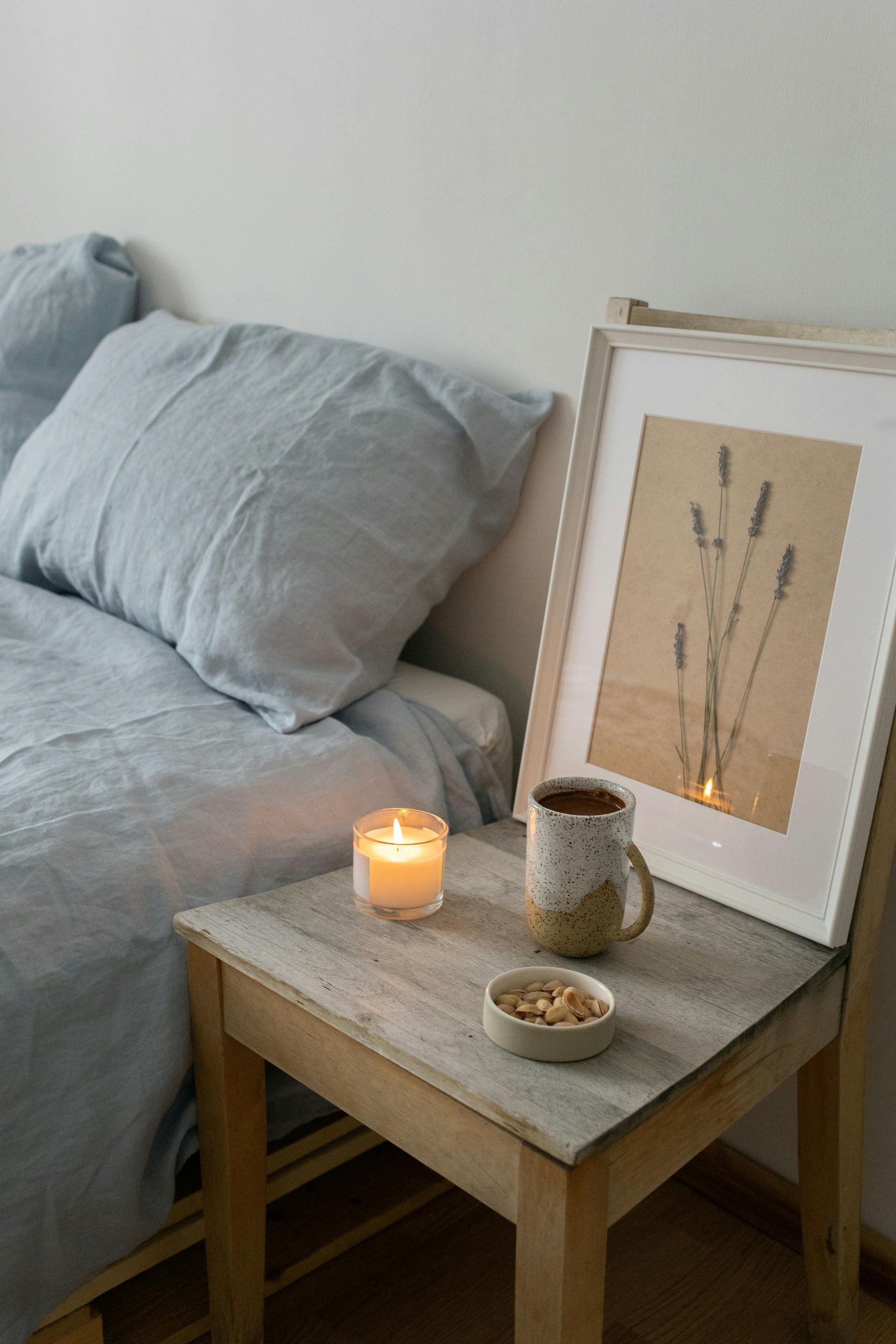 There is a candle and a cup of coffee on the nightstand next to the bed.